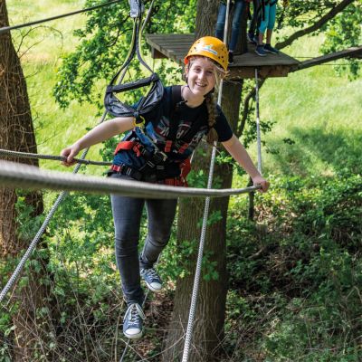Jugendliche mit Helm balanciert mit Sicherung in einem Schwebeelement