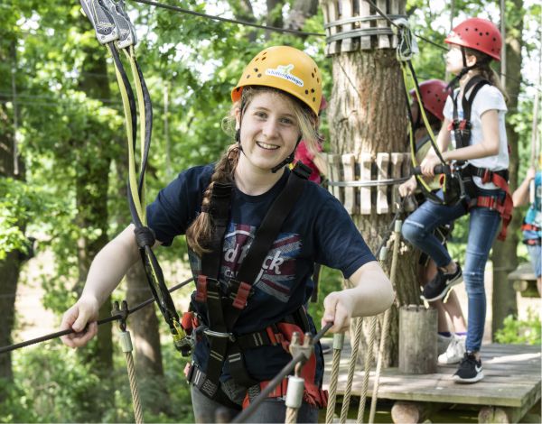 Drei Kinder mit Helm klettern gesichert in einem Kletterelement