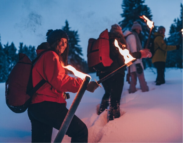 Eine Gruppe  junger Menschen wandern mit Fackeln durch tiefen Schnee 