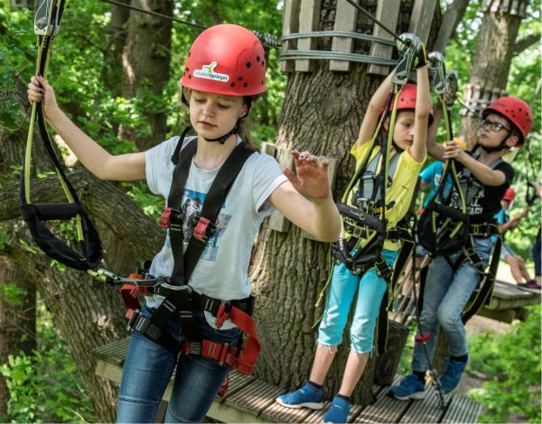 Drei Kinder mit Helm klettern gesichert in einem Kletterelement
