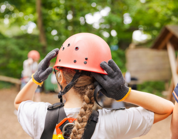 Drei Kinder mit Helm klettern gesichert in einem Kletterelement