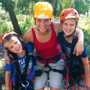 Junge Frau Arm in Arm mit zwei Kindern in Kletterausrstung lachen in die Kamera