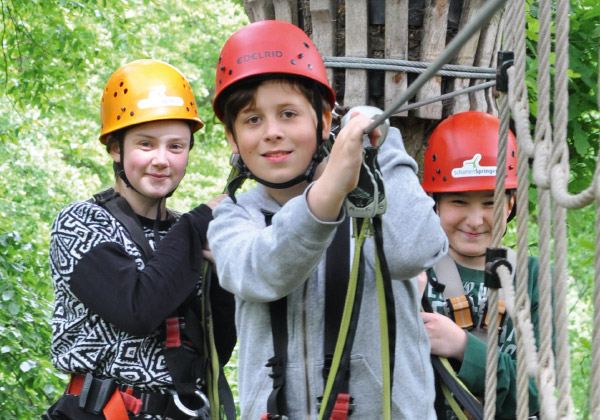 Drei Kinder mit Helm klettern gesichert in einem Kletterelement